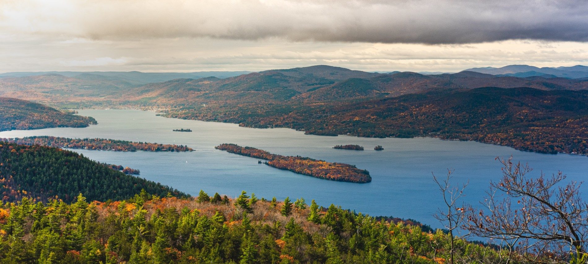 Overhead view of a large river nestled between forest covered mountains and cloudy skies overhead