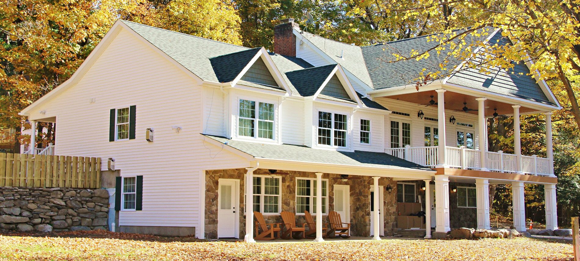 Exterior view of charming white house with stone accents; featuring numerous porches with cozy seating