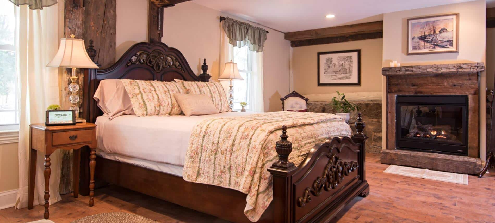 Guestroom features rustic wood fireplace and neatly made bed with white linens and cozy quilt 