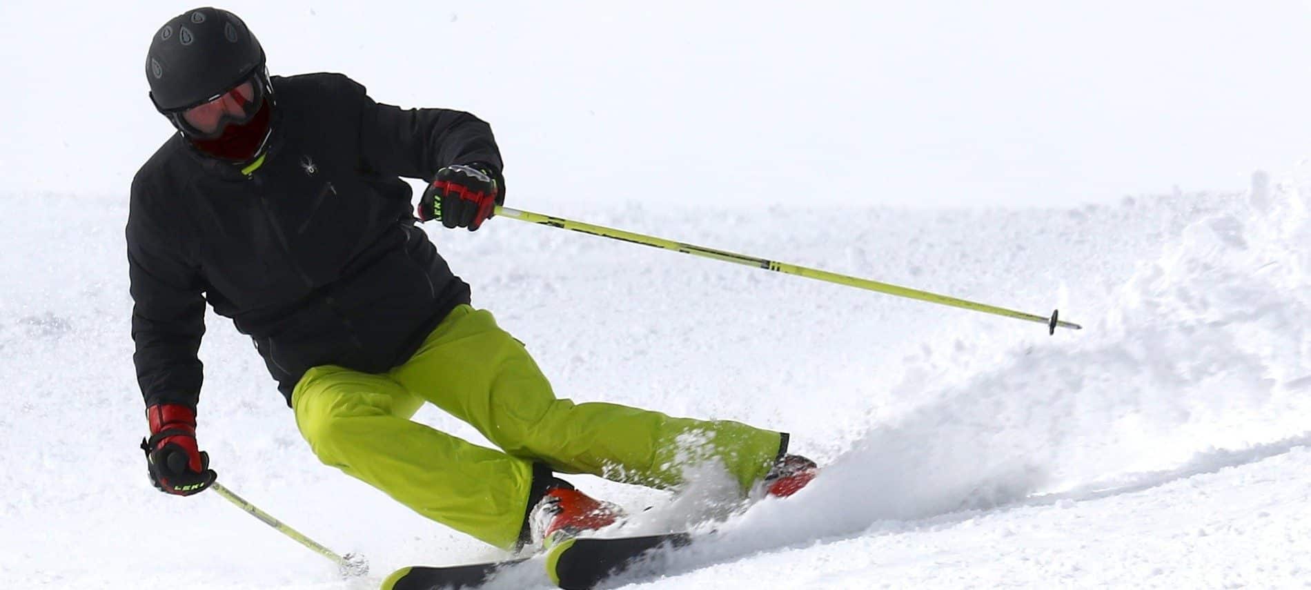 Man in black jacket and green snowpants on skis using poles to make a turn on a snow-covered hill