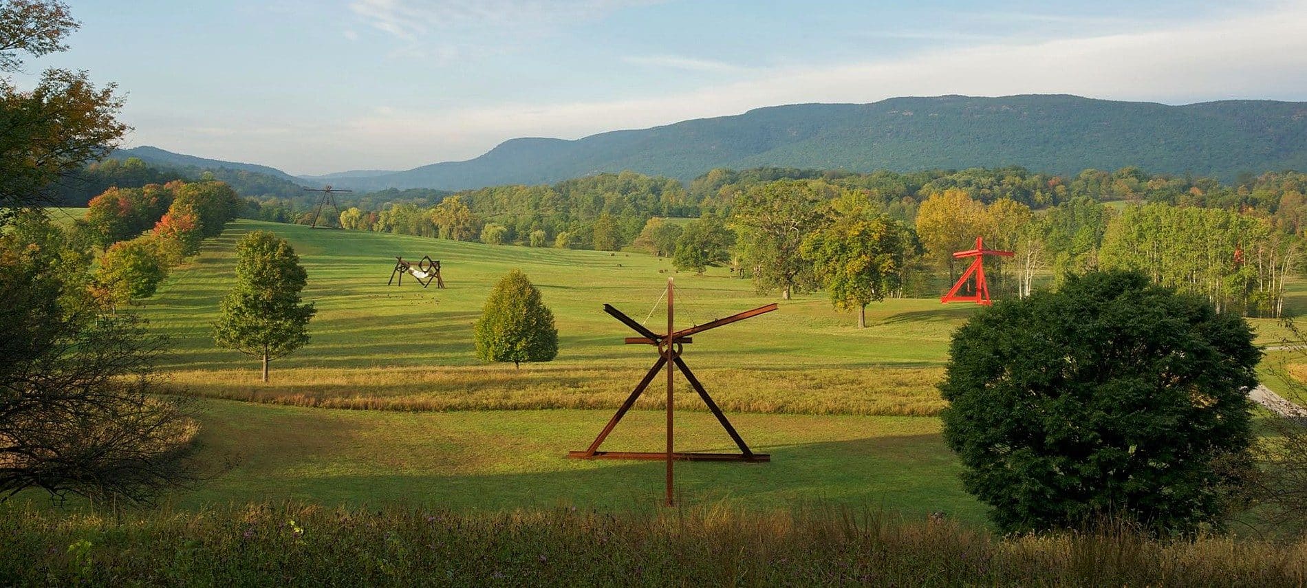 Expansive outdoor park lush open space, trees and mountains and several art sculptures