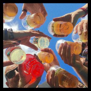 A group of people, mostly just hands showing, holding plastic cups of light beer
