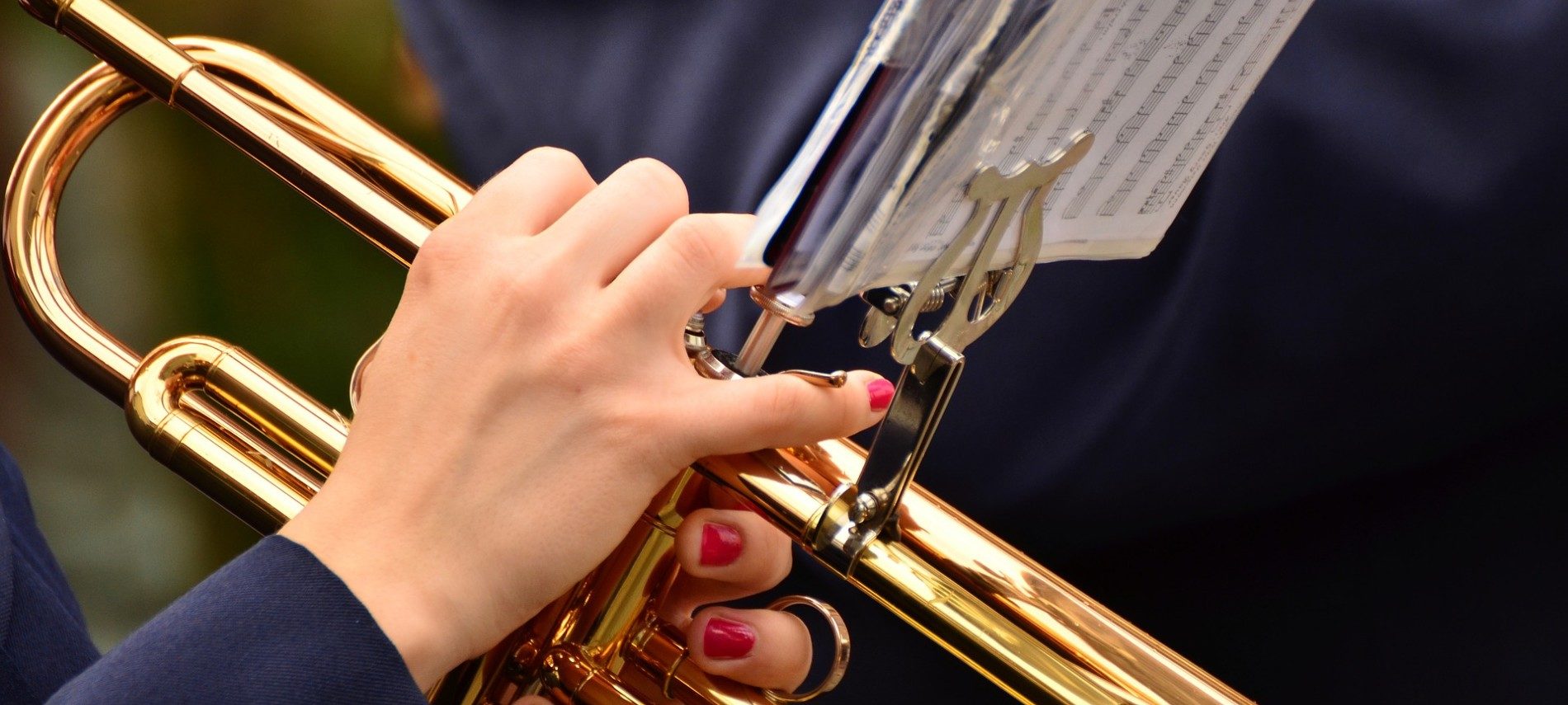 Woman in a dark suit holding a gold brass trumpet with white sheet music attached
